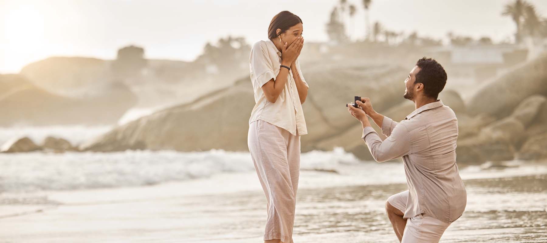 Ein Mann kniet vor seiner Traumfrau und macht Ihr einen Heiratsantrag am Strand